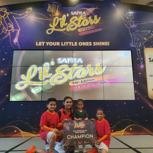 Four smiling family members kneeling together on stage holding up their SAFRA Lil Stars Vocal Families for Life Category Champion board