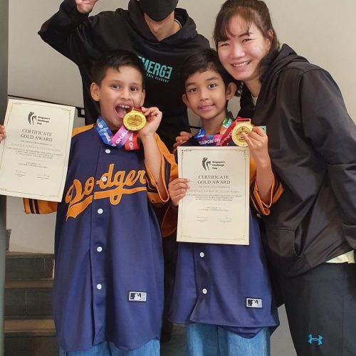 Two smiling dance coaches posing beside two excited young boys holding gold competition certificates and medals