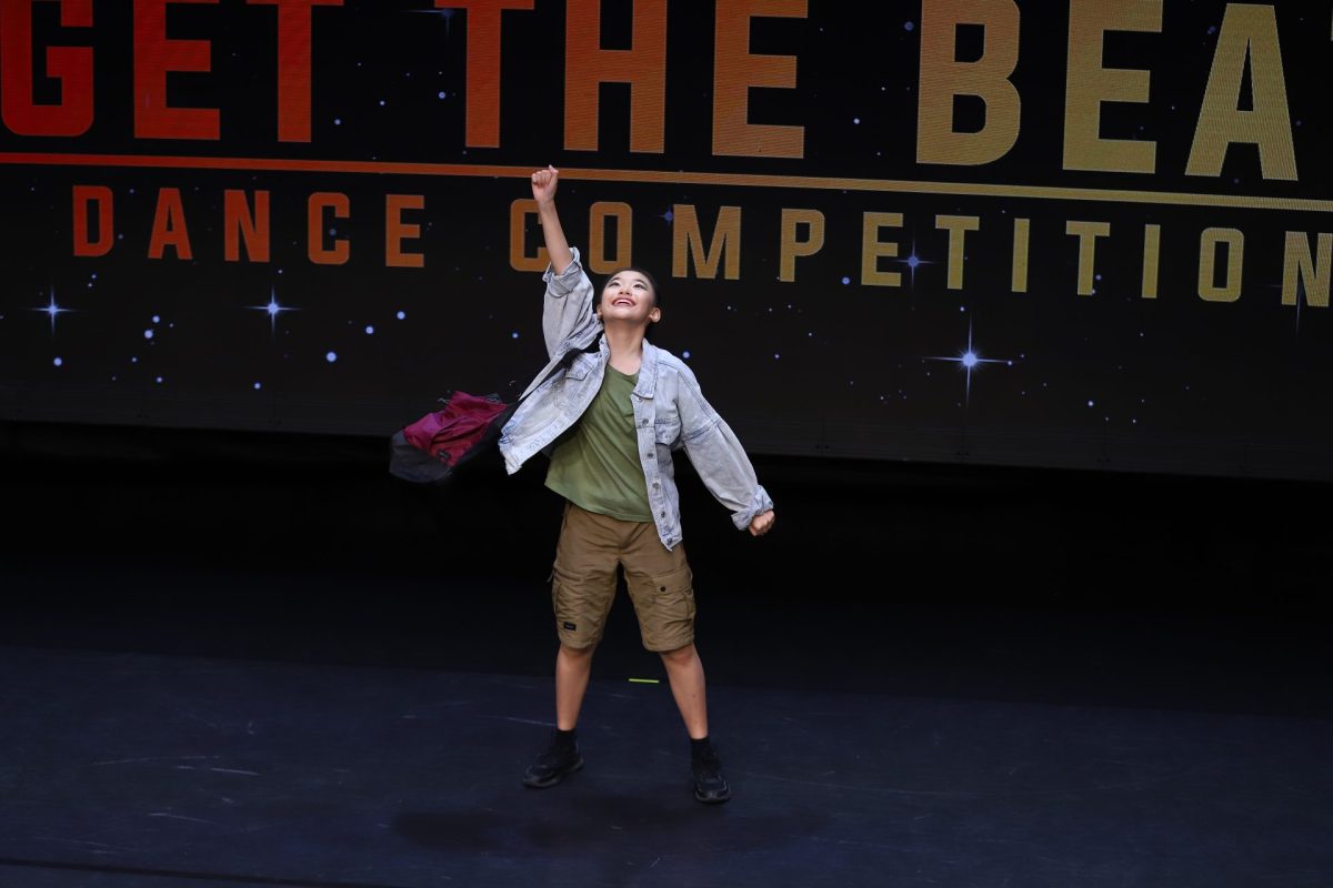 A young dancer poses on stage with one fist raised during a dance competition