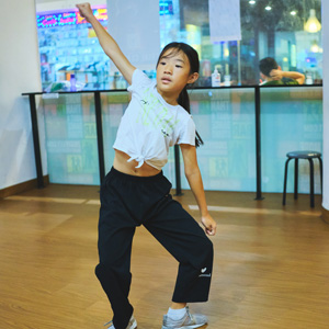 Young dancer striking an energetic pose with one fist raised and one leg bent during dance practice in a studio