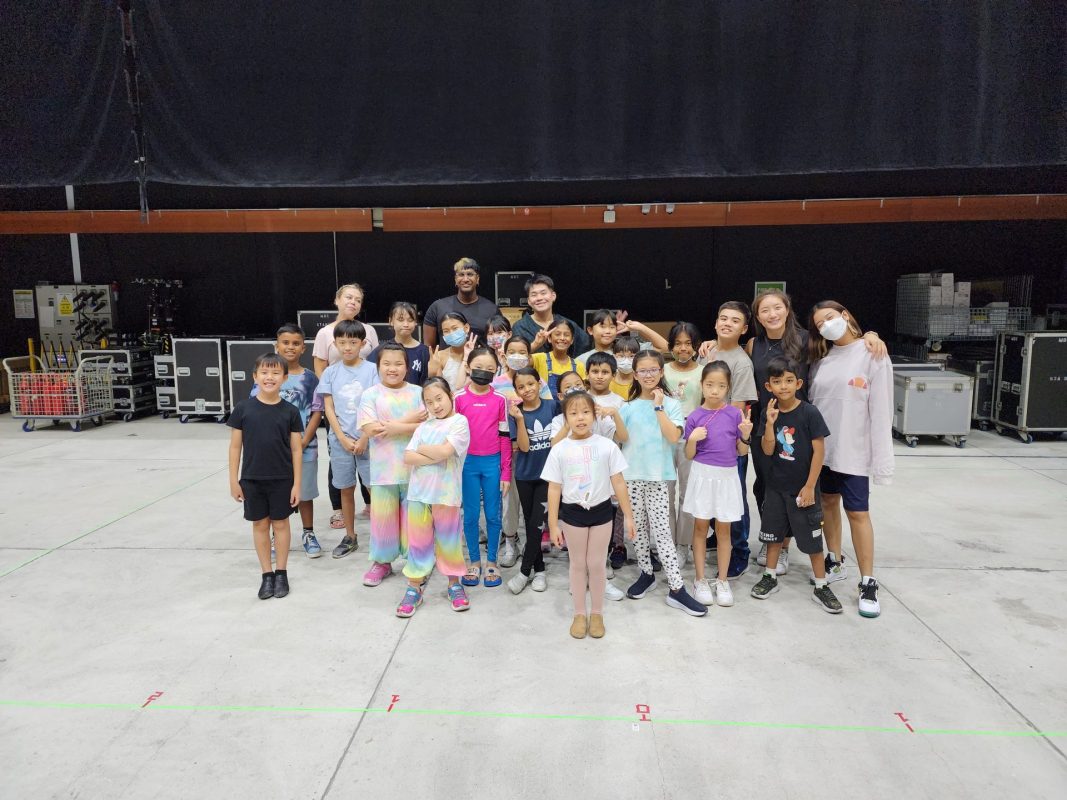 group of children and instructors smile and pose together on the backstage floor