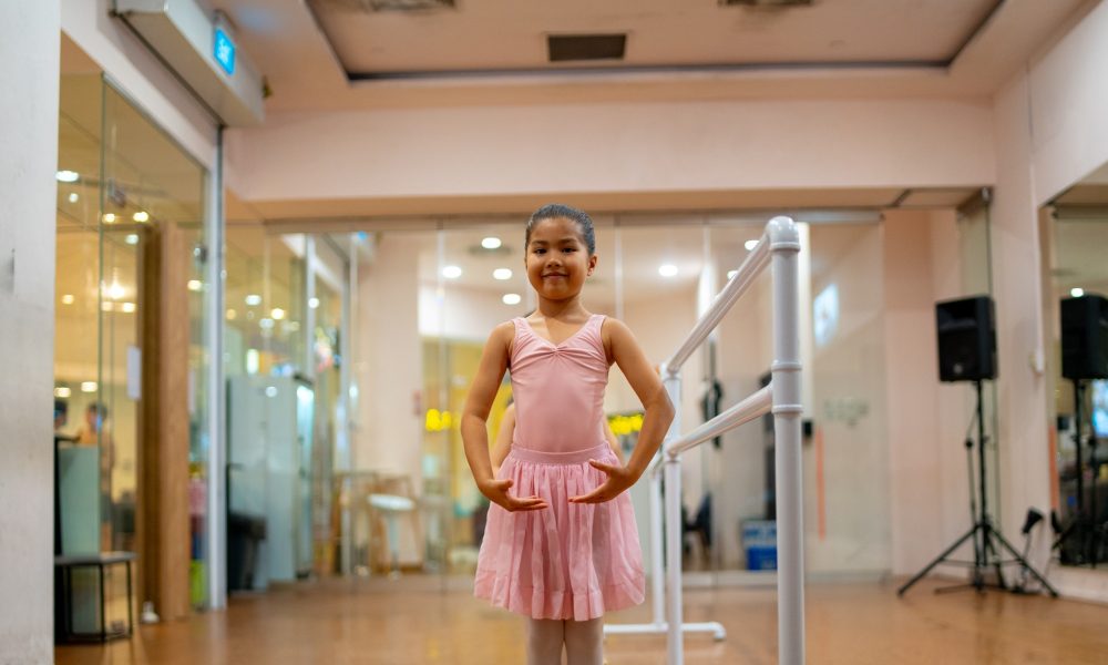 young-ballerina-practicing-first-position-at-ballet-barre Young girl in a pink leotard and ballet tutu standing in first position near a white ballet barre in a dance studio
