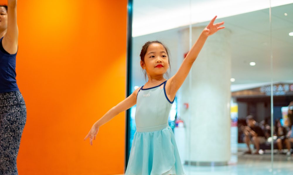 young-ballerina-practicing-graceful-pose A young girl in a light blue ballet dress holding a graceful arm pose during a dance lesson in a studio