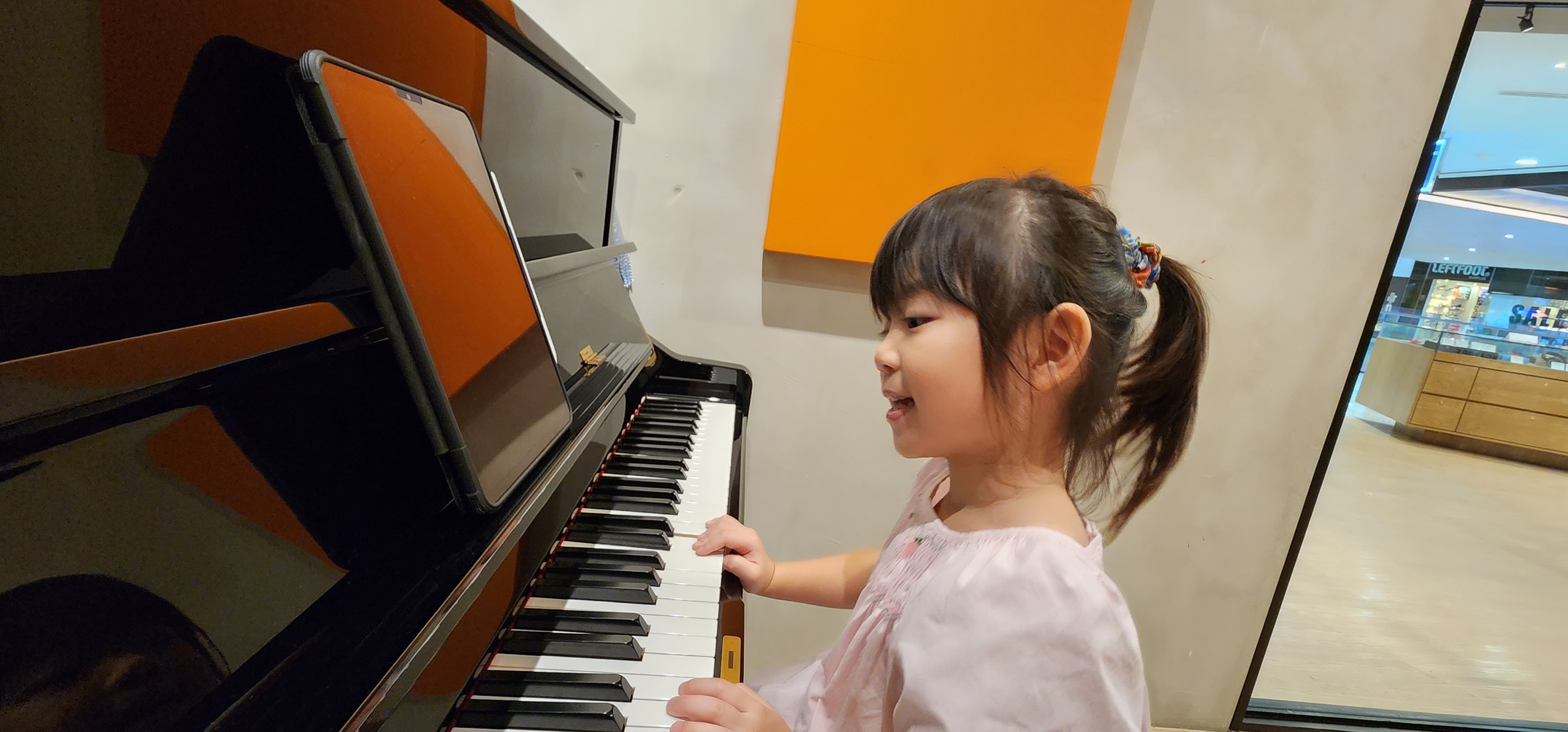 A young girl smiles while playing an upright acoustic piano
