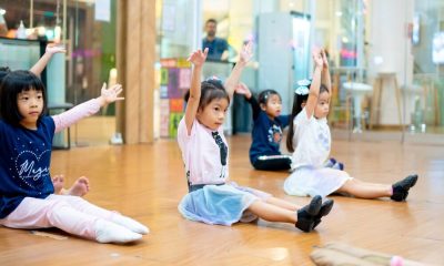 children-warm-up-stretch-dance-class-studio-floor Young girls sitting on a wooden studio floor raising their arms during a dance warm up routine