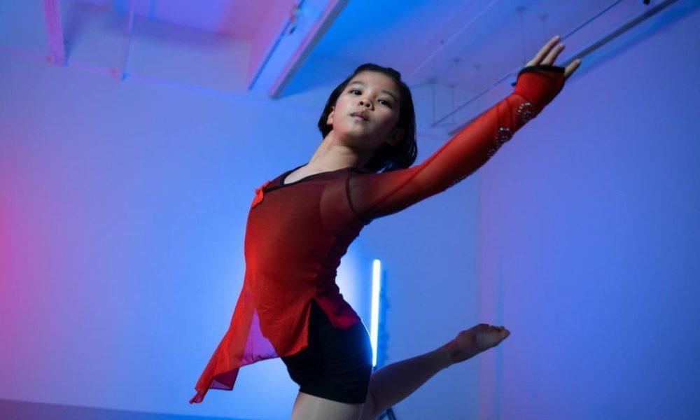 Young female dancer wearing a red sheer outfit performing an expressive leap under cool blue studio lighting