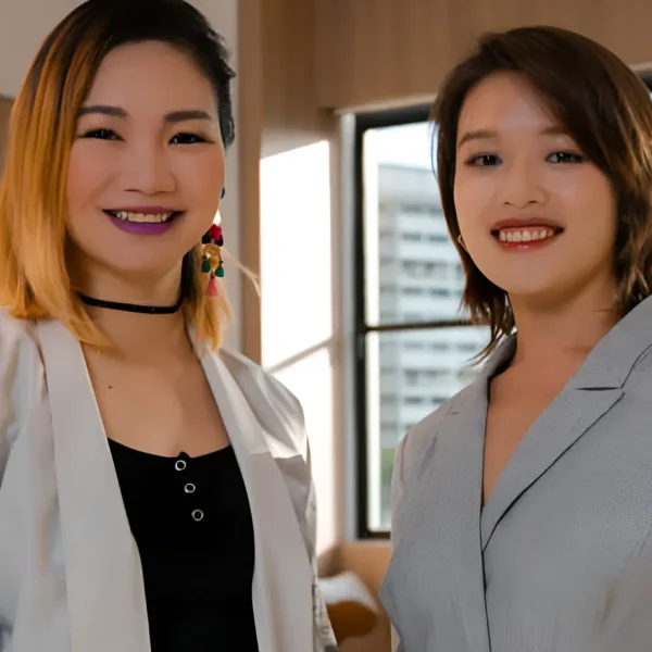 Two smiling professional women standing side by side indoors near a window