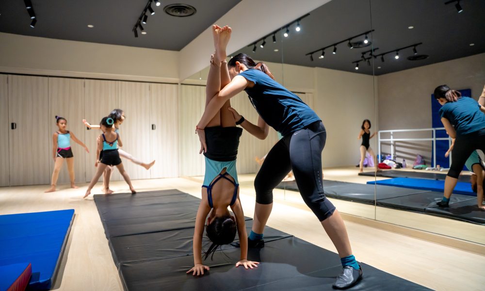 dance-instructor-assisting-student-handstand-pose Dance instructor helping a young girl hold a stable handstand position during training class
