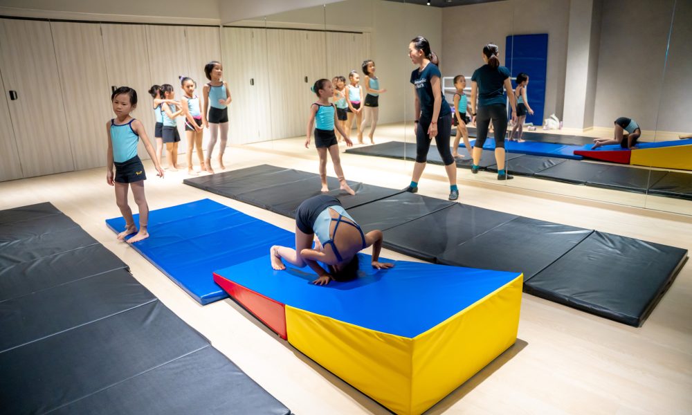 kids-acrobatic-gymnastics-class-somersault-practice Children in a gymnastics studio practicing forward rolls and somersaults over a soft incline wedge mat
