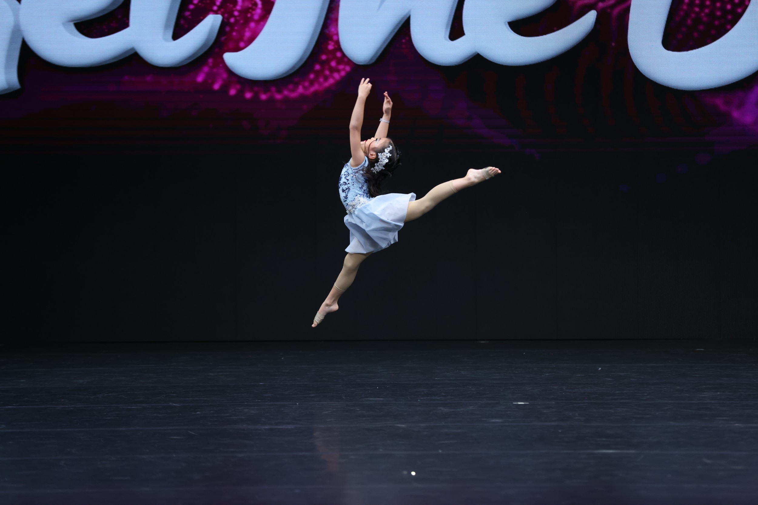 young-solo-dancer-performing-mid-air-leap-onstage A young dancer in a light blue dress leaps gracefully in mid-air during a solo stage performance