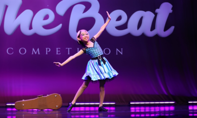 young-girl-performing-dance-on-stage-at-the-beat-competition Young girl in a blue polka dot dress performing a dance routine on stage at The Beat competition with a guitar case beside her